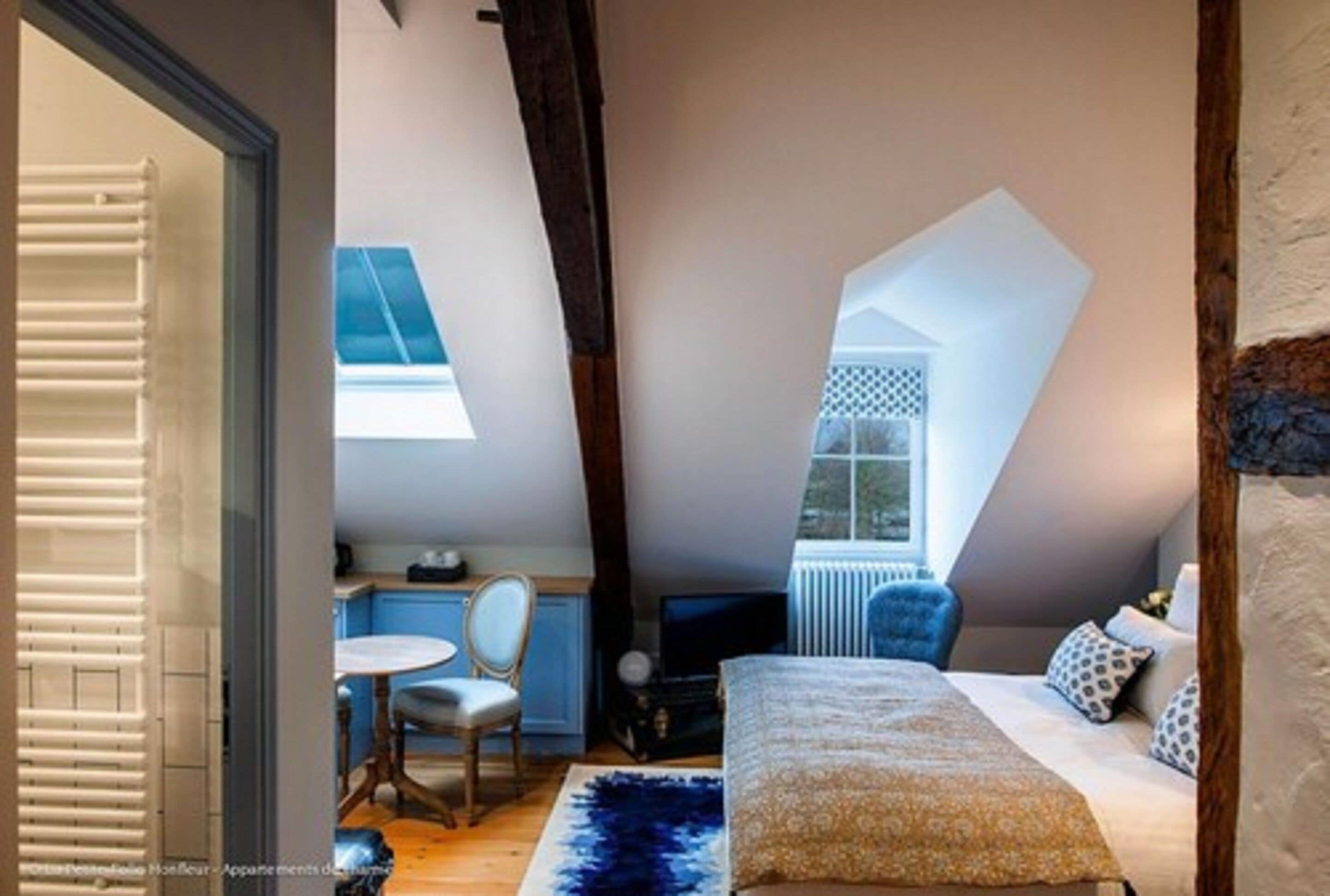A bedroom with a sloped ceiling, a bed, a chair, a table, and a window.