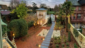A garden pathway leading to a small tower-like structure, surrounded by well-maintained hedges and plants. - La Petite Folie (Honfleur)
