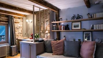 A cozy room with a stone wall, wooden beams, a built-in bench, and shelves with books and a bicycle.