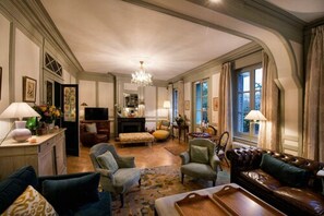A spacious living room with a fireplace, comfortable seating, and a chandelier. - La Petite Folie (Honfleur)