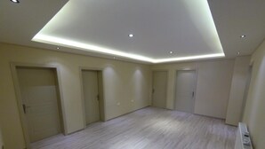 Een ruime kamer met een hoge plafond, inbouwverlichting en een lichtkleurige houten vloer.