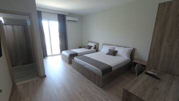 Una habitación de hotel moderna con dos camas, un escritorio de madera y un ventanal corredero que da a un balcón.