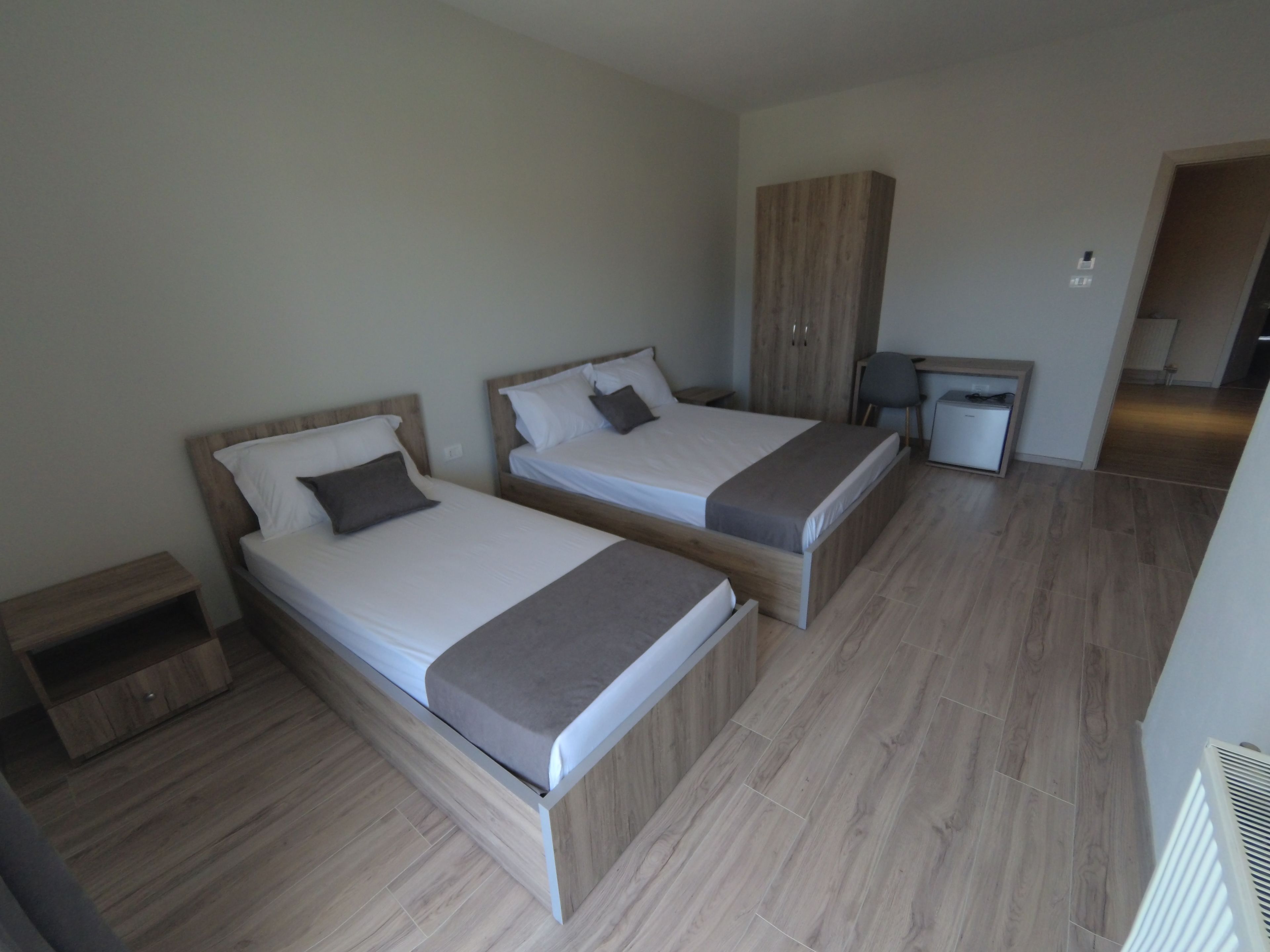 Une chambre moderne avec deux lits simples, une armoire en bois, une petite table de chevet et un bureau avec une chaise.