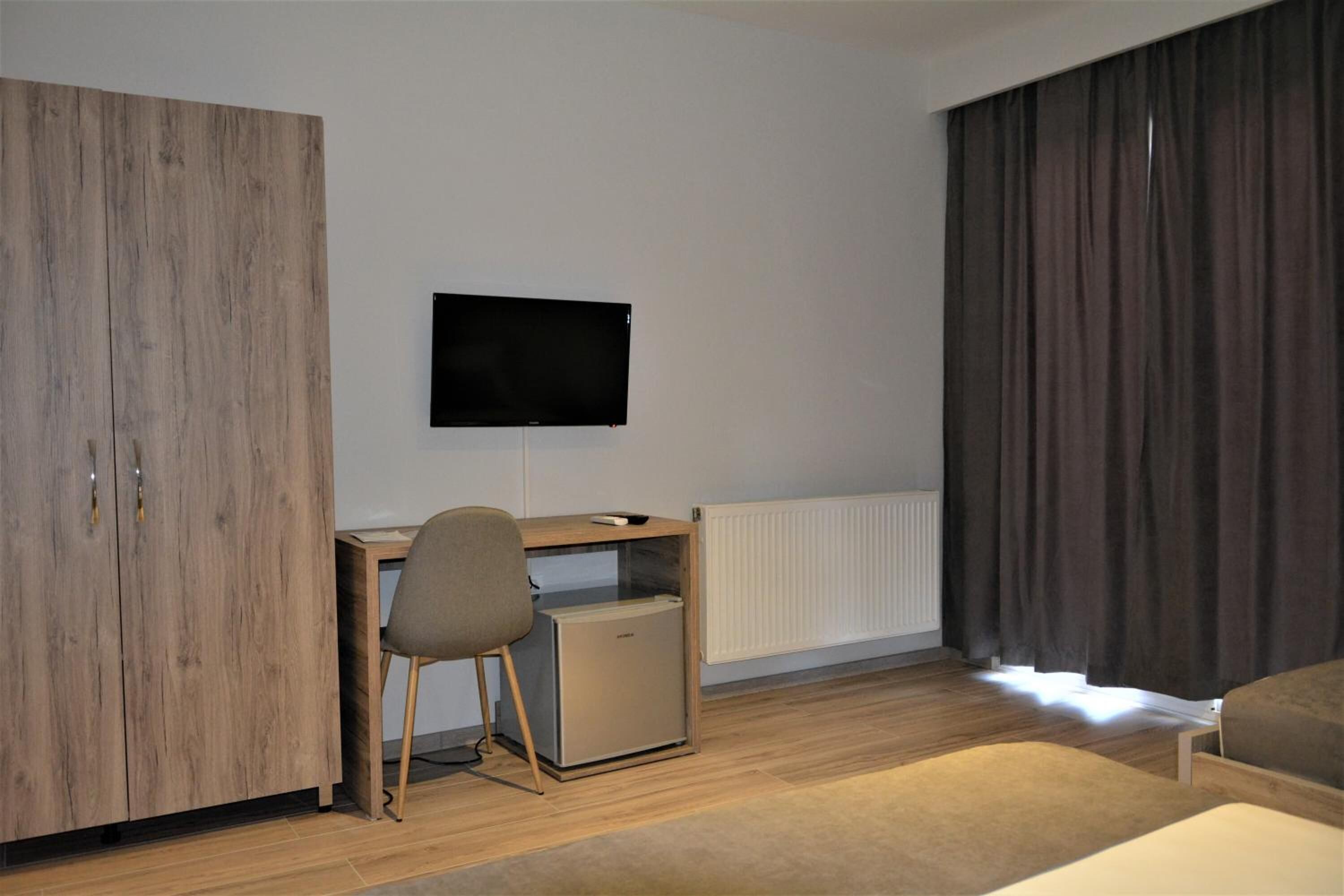 Un dormitorio con un armario de madera, un escritorio con silla, un televisor y una cama.