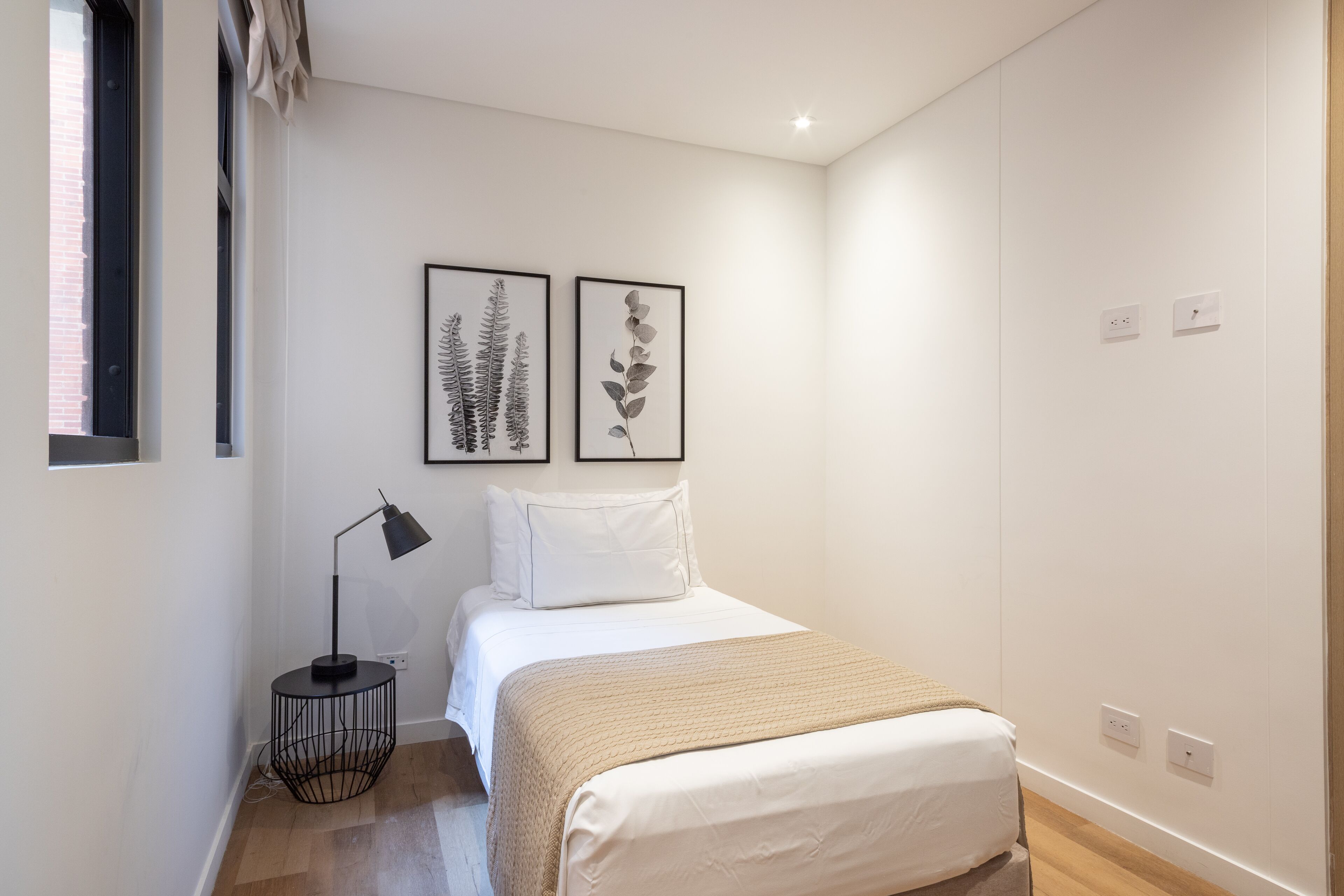 Ein Schlafzimmer mit einem Bett, einer Nachttischlampe und zwei gerahmten Pflanzenmotiven an der Wand.