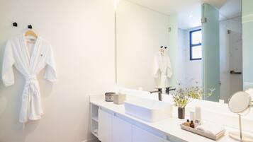 A modern bathroom with a white vanity, a large mirror, and a robe hanging on the wall.
