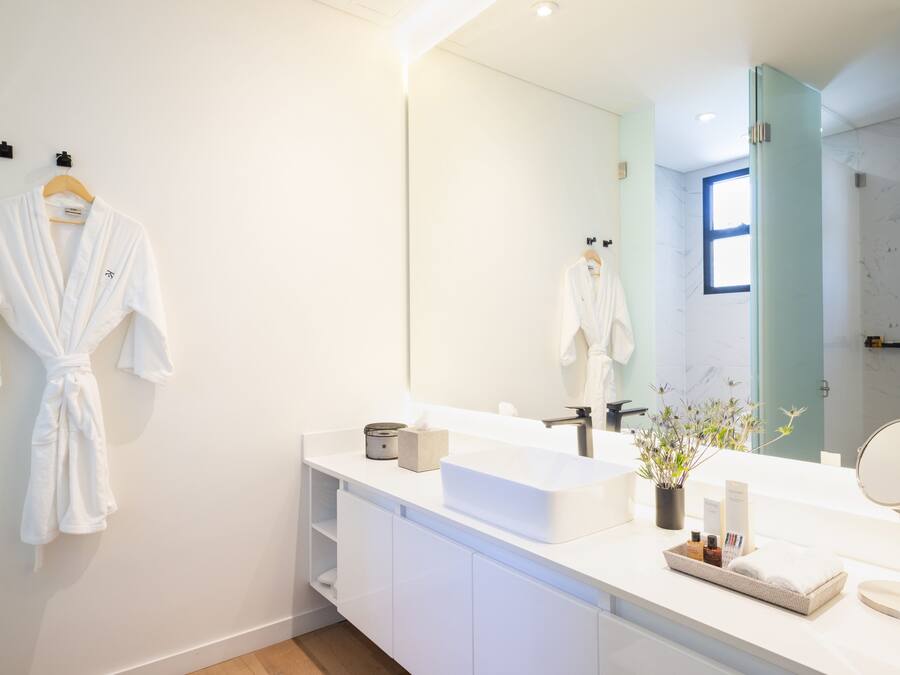 A modern bathroom with a white vanity, a large mirror, and a robe hanging on the wall.