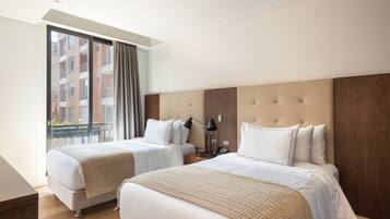 Een hotelkamer met twee bedden, een groot raam met gordijnen, een houten hoofdbord en uitzicht op een gebouw.