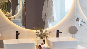 A modern bathroom with a large mirror, two sinks, and a robe hanging on a rack.