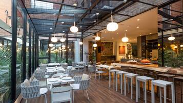 A modern restaurant with high ceilings, large windows, and a variety of seating arrangements including tables and bar stools.
