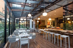 A modern restaurant with high ceilings, large windows, and a variety of seating arrangements including tables and bar stools.
