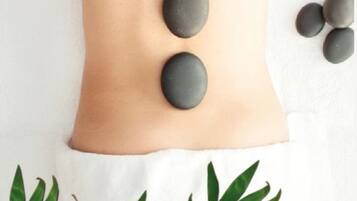 A person receiving a back massage with stones placed along their spine on a white towel.