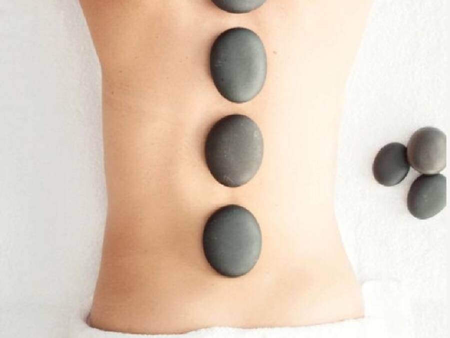 A person receiving a back massage with stones placed along their spine on a white towel.