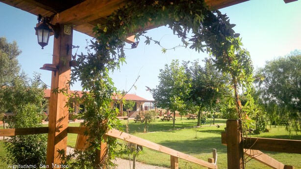 A wooden pergola with climbing plants, a picnic area, and a view of a building with a red roof.