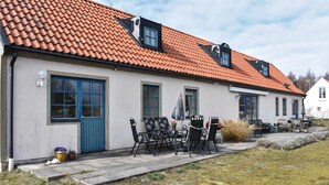 A two-story building with a red-tiled roof, a blue door, and a patio with outdoor furniture. - 3 bedroom nice home in Borrby (Borrby)