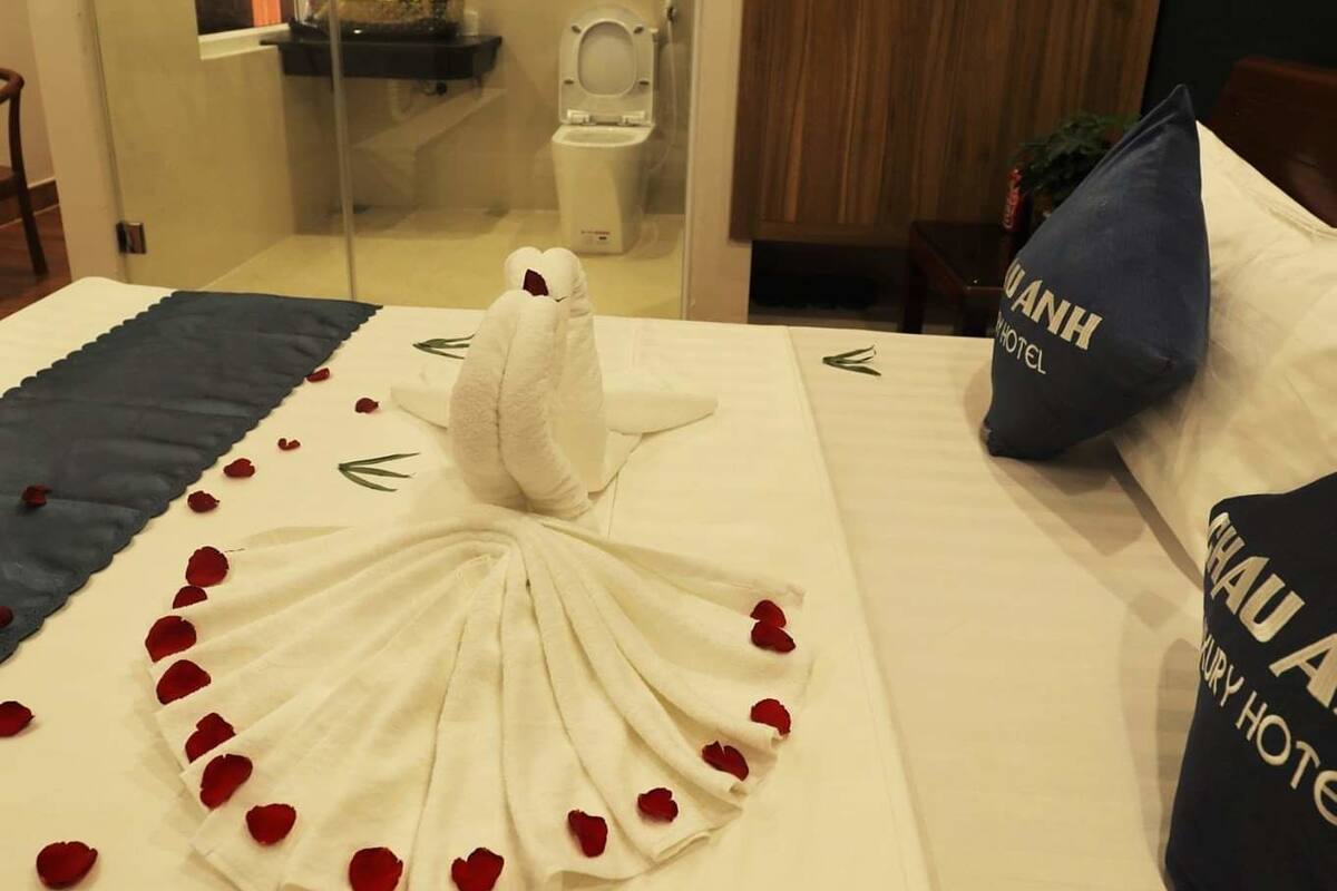 Ein Hotelzimmer mit einem Bett, das mit Rosenblättern und einer weißen Schwan-Dekoration geschmückt ist, einem Holzschrank, einer Duschkabine aus Glas und einem sichtbaren Badezimmer.