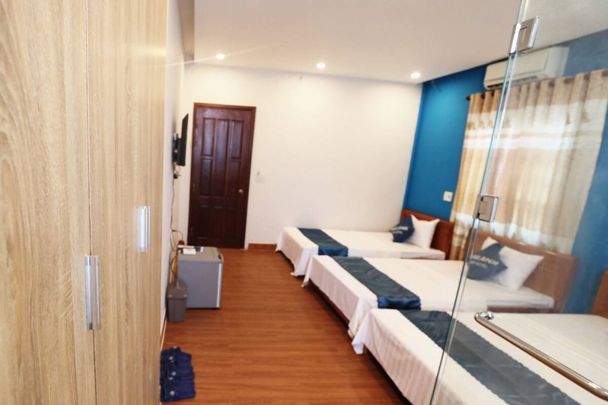 Ein Hotelzimmer mit zwei Einzelbetten, einem Kleiderschrank, einem Schreibtisch und einer kleinen Mülltonne.