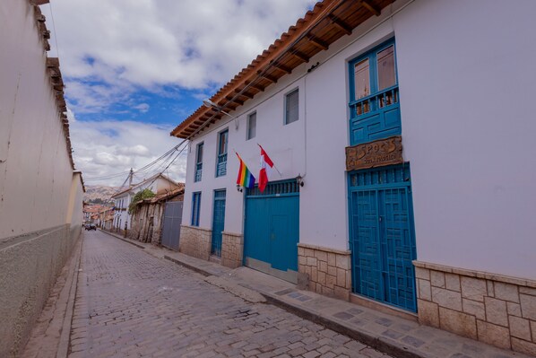 A narrow cobblestone street lined with white buildings featuring blue doors and windows. - Hawka Inka Hostal (Cusco)