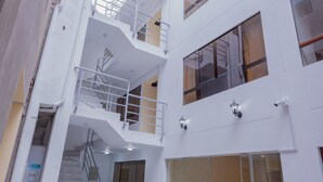 A multi-level building with a central staircase, glass doors, and a small outdoor area with a potted plant. - Hawka Inka Hostal (Cusco)