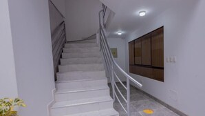 A staircase with white marble steps and a metal railing, leading to a landing with a wooden panel wall and a light fixture. - Hawka Inka Hostal (Cusco)