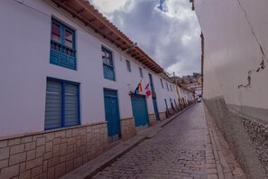 A narrow cobblestone street flanked by white buildings with blue shutters and doors. - Hawka Inka Hostal (Cusco)