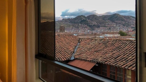 A view from a window overlooking a cityscape with terracotta rooftops and a mountain in the background. - Hawka Inka Hostal (Cusco)