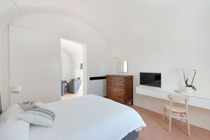 A bedroom with a bed, a wooden dresser, a desk with a chair, a television, and a potted plant. - Masseria Pensato SUITE CARRUBO (Fasano)