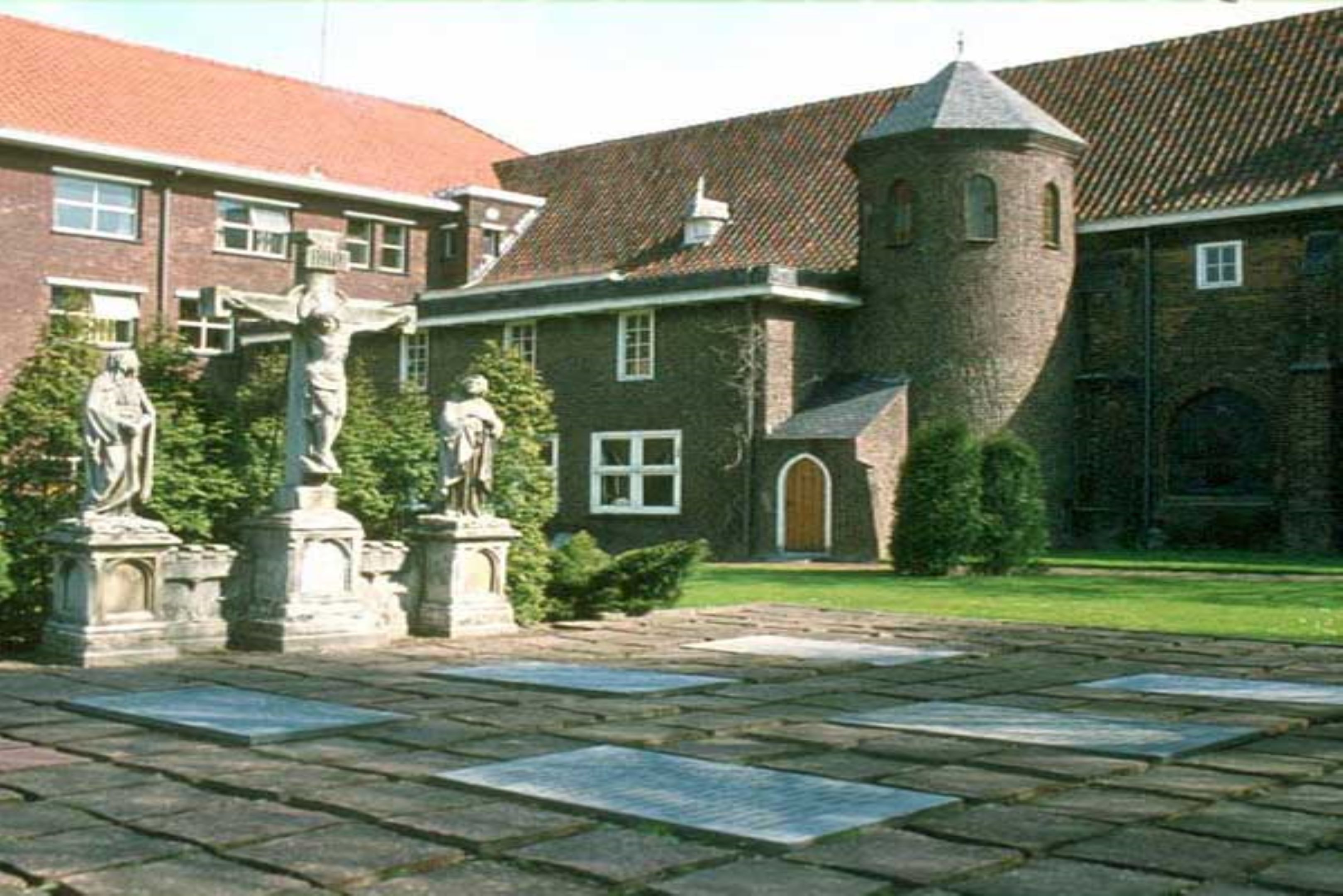 A courtyard with stone statues, a brick building with a tower, and a red-tiled roof.