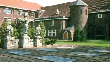A courtyard with stone statues, a brick building with a tower, and a red-tiled roof.