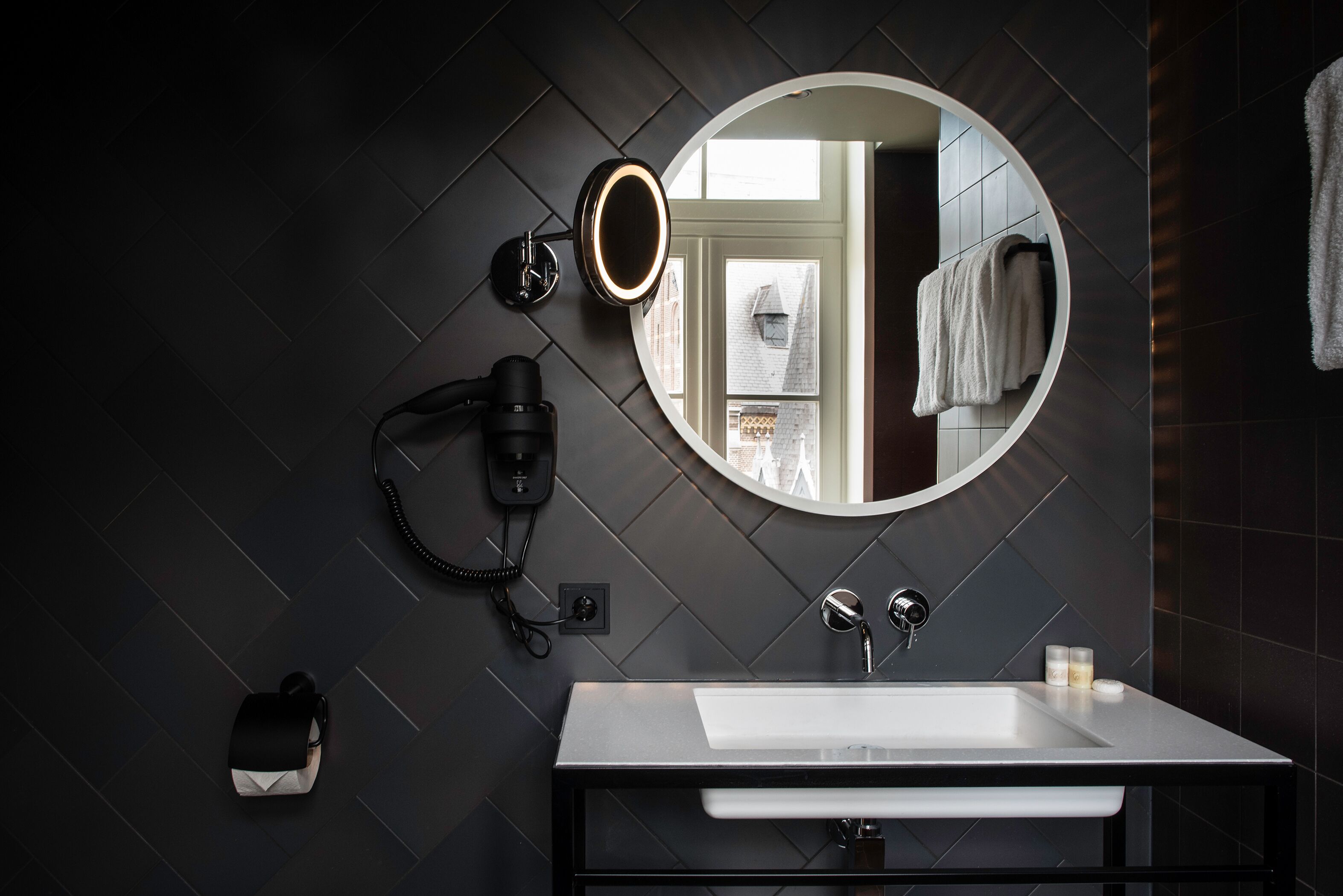 Un baño moderno con un espejo grande, un lavamanos blanco y un secador de pelo en la pared.