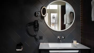 Un baño moderno con un espejo grande, un lavamanos blanco y un secador de pelo en la pared.