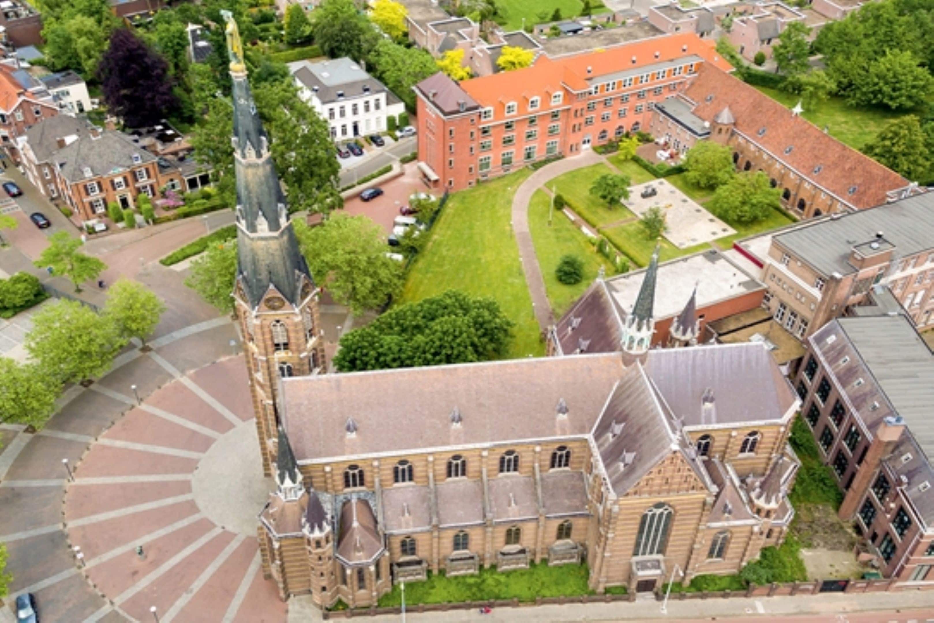 An aerial view of a historic building with a prominent tower, surrounded by a well-maintained courtyard and adjacent residential buildings.