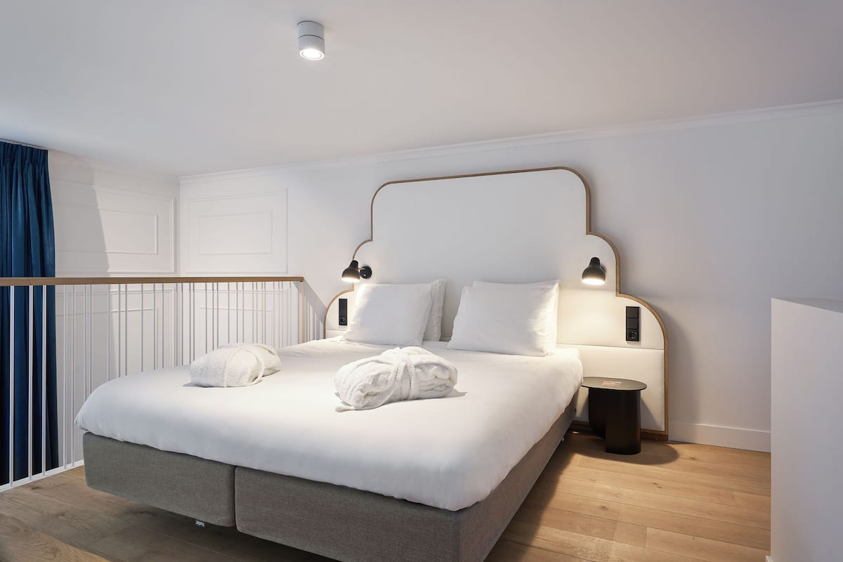 A modern hotel room with a large bed, two bedside tables, and a small bedside lamp.