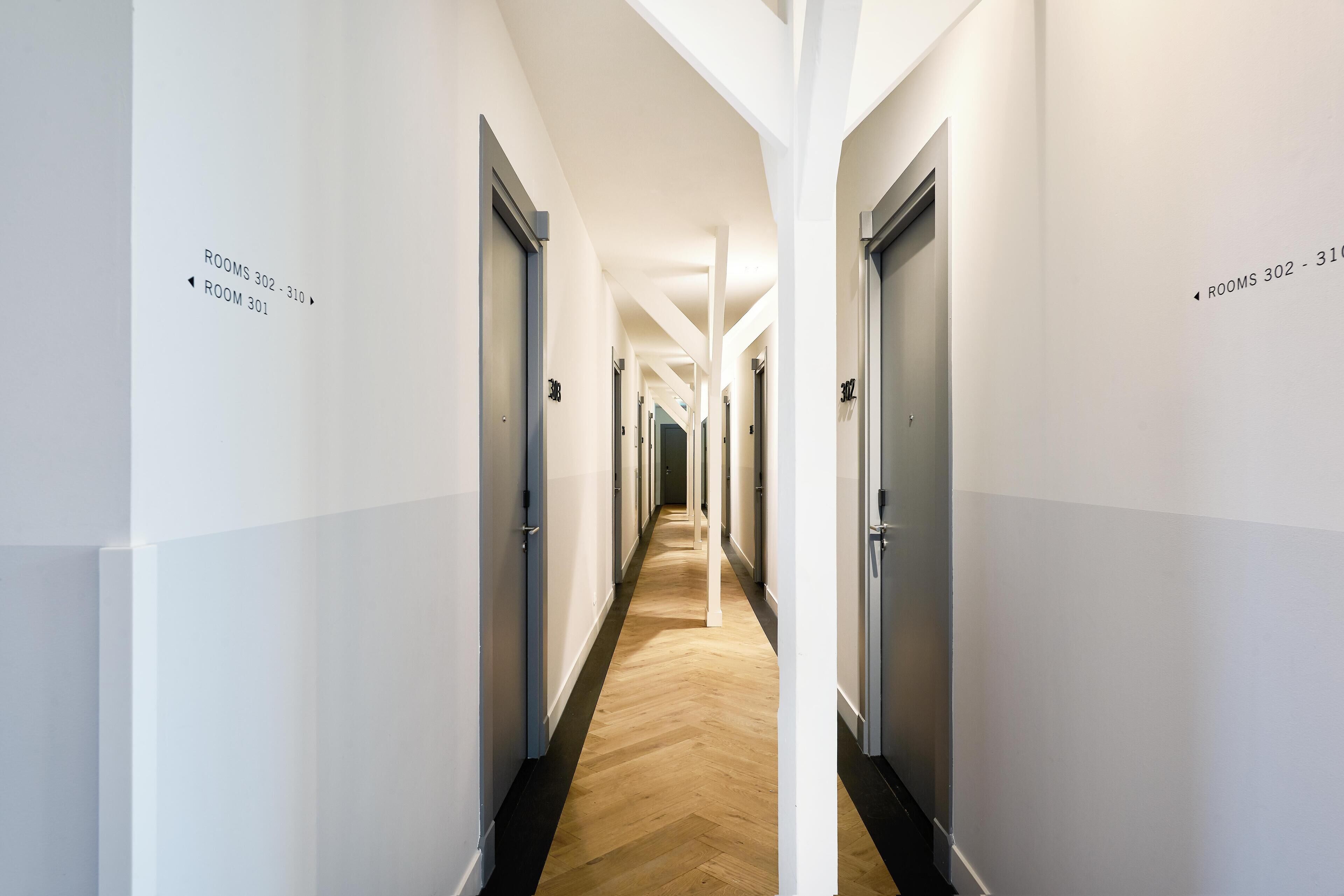 Un long couloir étroit, dont les portes sont marquées des numéros « 302-310 » et « 301 ».