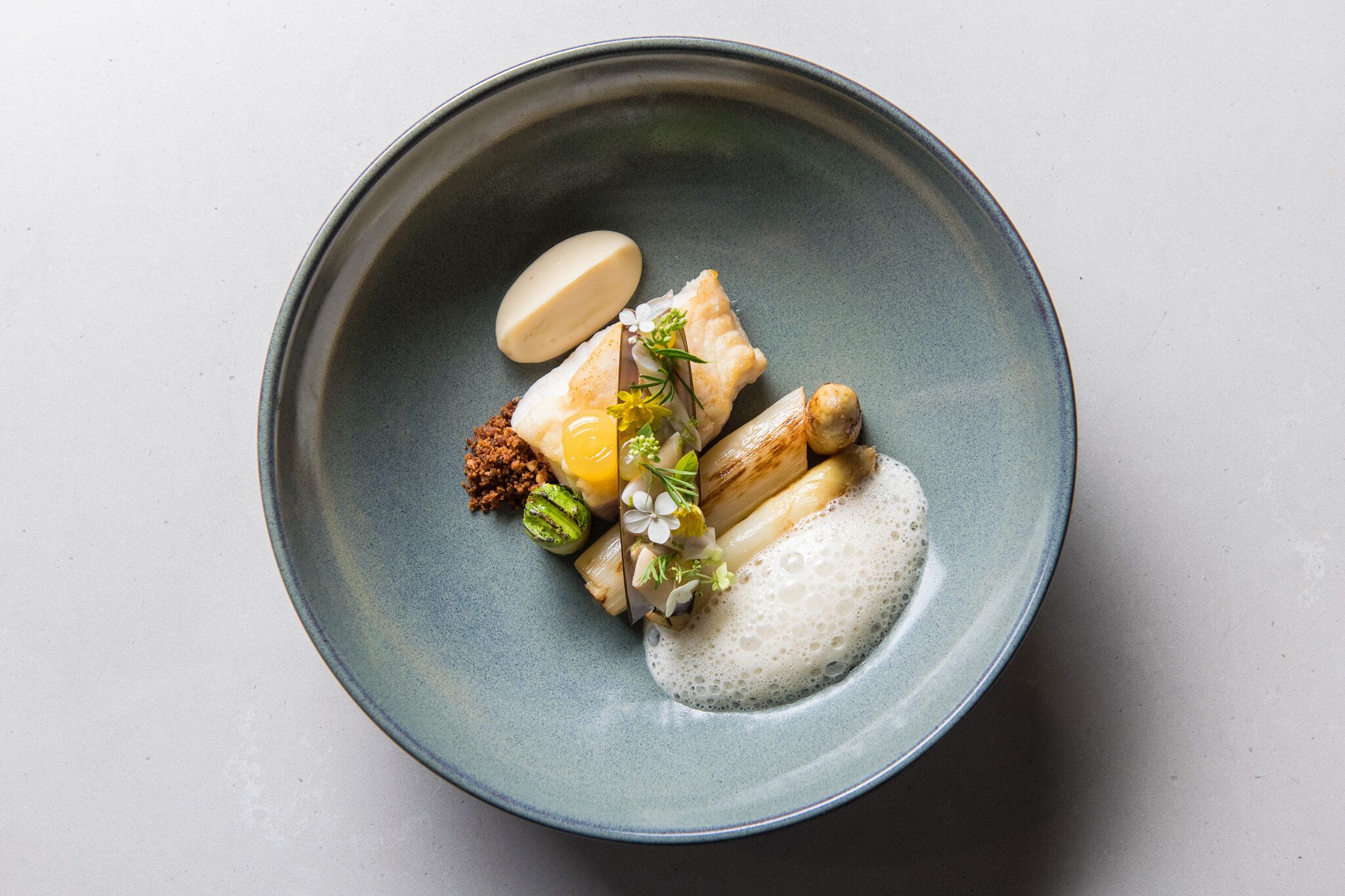 A round ceramic plate with a variety of food items including fish, rice, and a dollop of sauce.