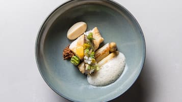 A round ceramic plate with a variety of food items including fish, rice, and a dollop of sauce.