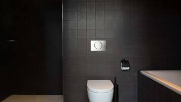 Un baño moderno con inodoro blanco, paredes de azulejos oscuros y un mecanismo de descarga a la vista.