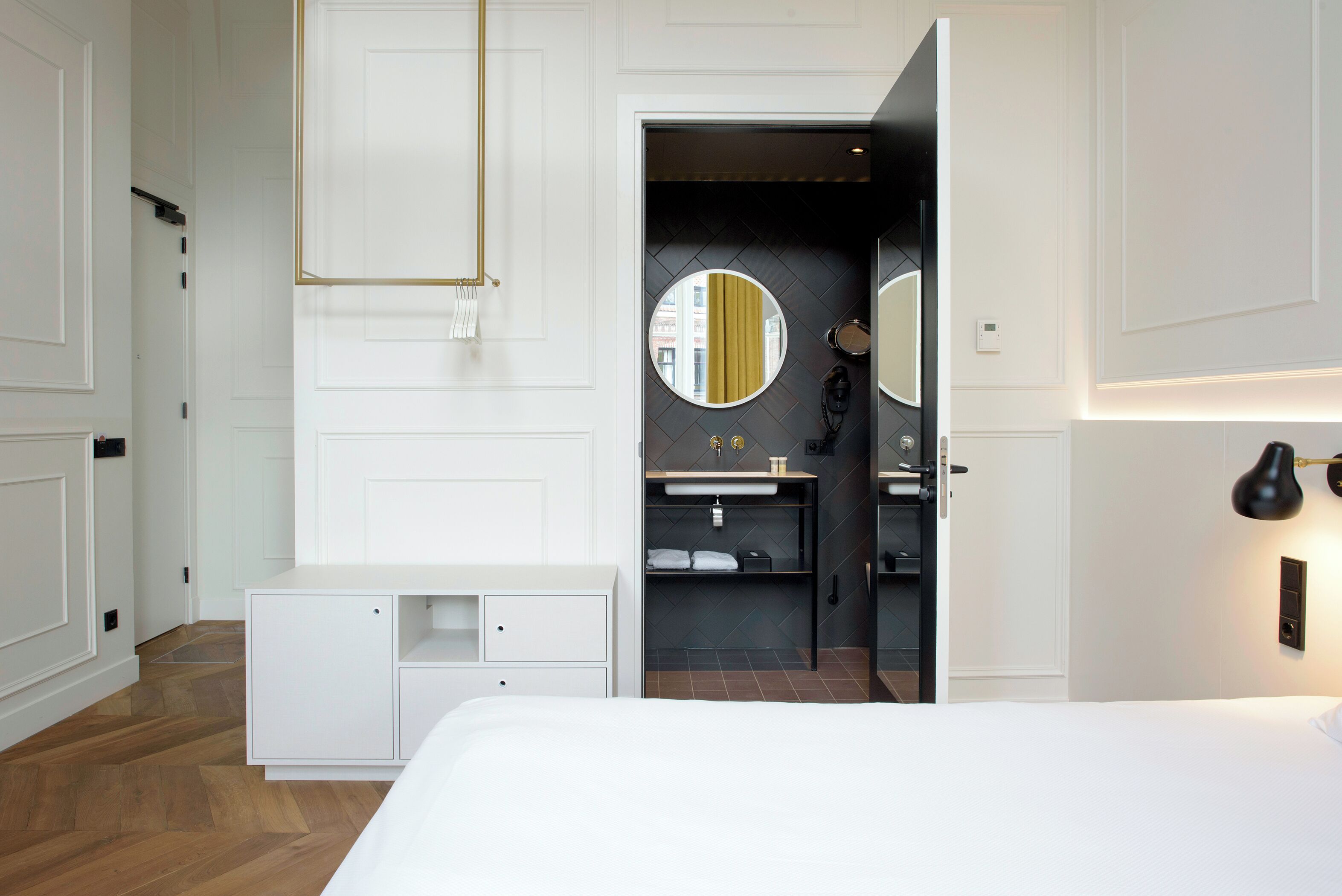 Ein modernes Hotelzimmer mit einem großen Bett, einem weißen Schrank, einem eingebauten Schminktisch mit Spiegel und einer kleinen Sitzecke.