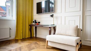 A room with a sofa, a TV mounted on the wall, a table with a lamp, and a window with curtains.