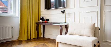 Una habitación con sofá, televisor montado en la pared, mesa con lámpara y ventana con cortinas.