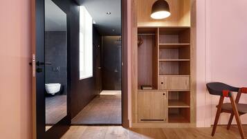Un baño moderno con inodoro, lavabo y zona de ducha. Se observa un mueble de madera con estantes y un aplique colgante.
