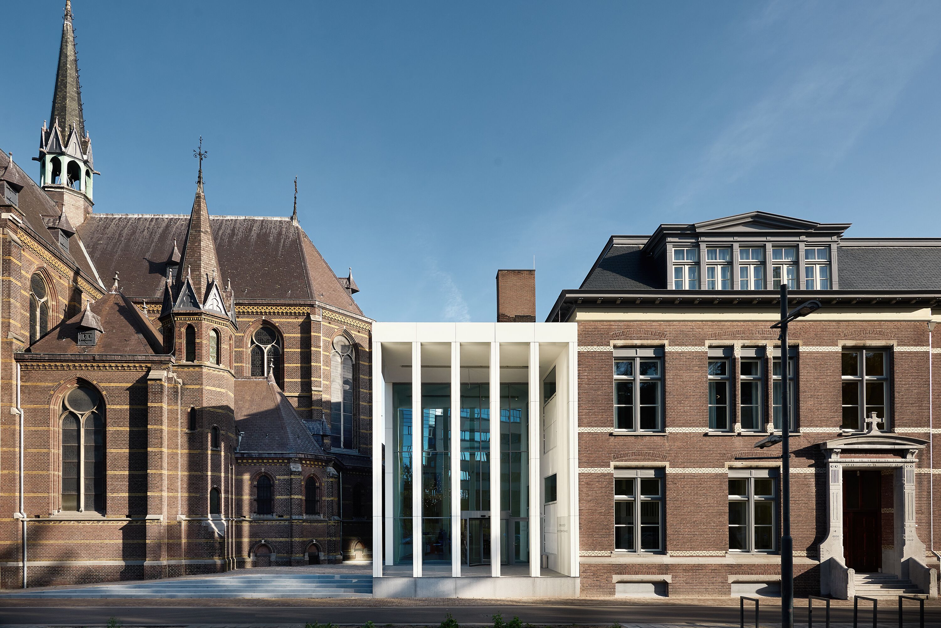 En historisk kirke med en moderne glasklædt indgang og en tilstødende traditionel murstensbygning.