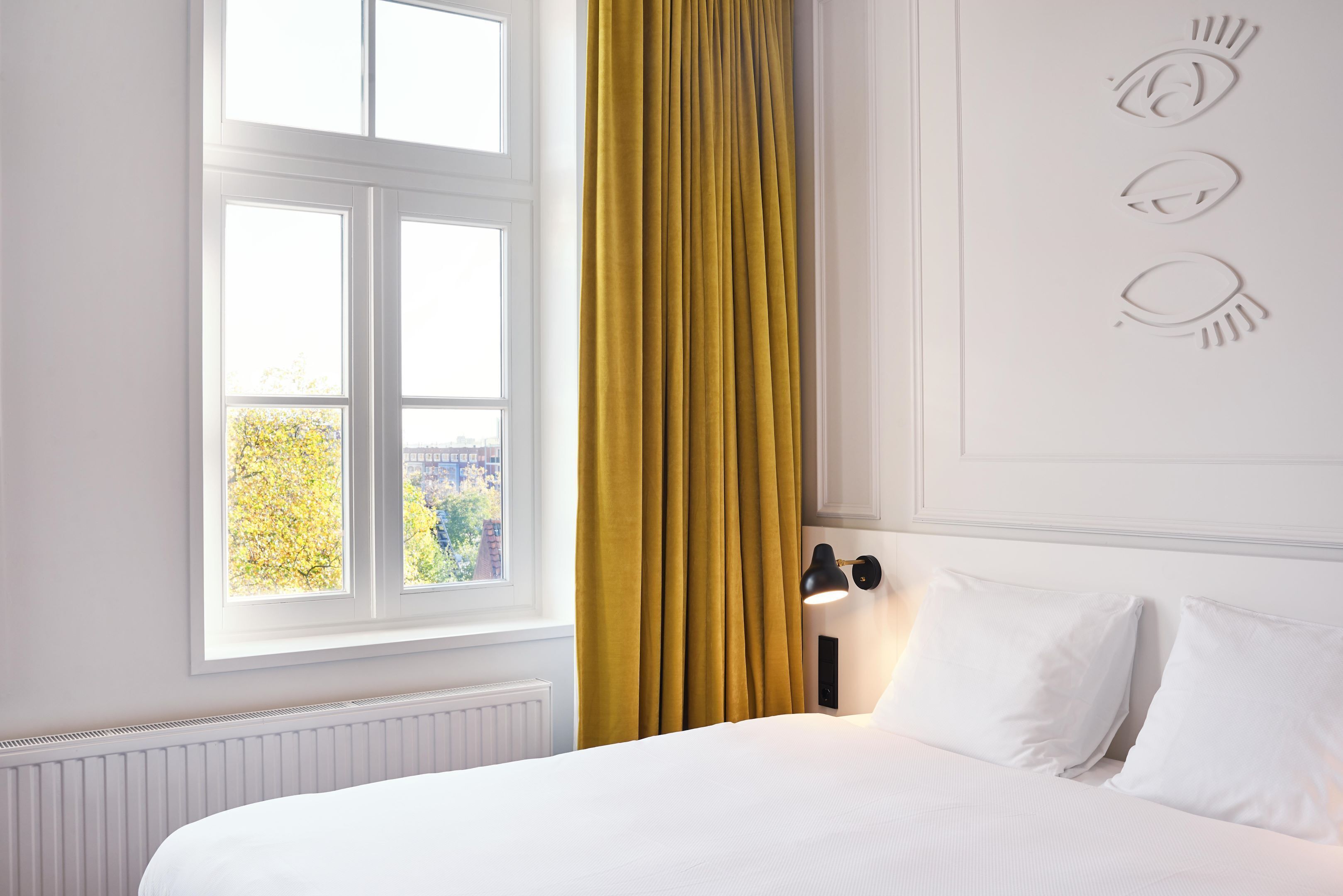 A hotel room with a bed, a window with curtains, and a wall with decorative elements.