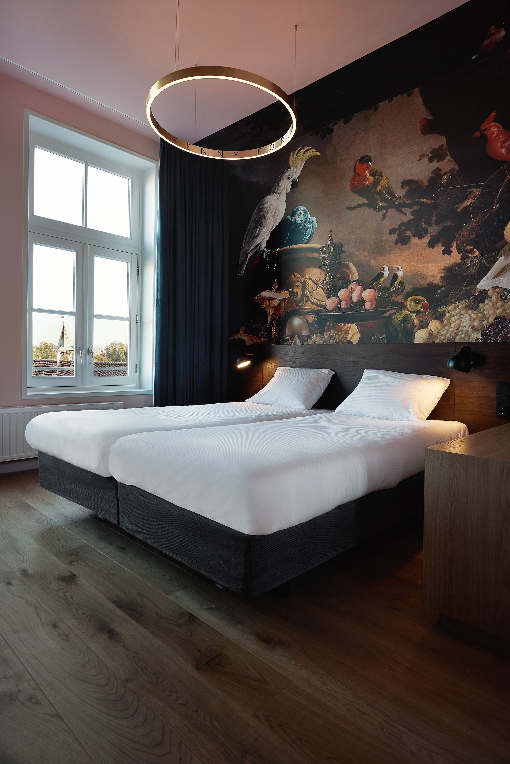 Un lit double avec du linge de lit blanc, une tête de lit sombre et une fresque murale représentant des oiseaux et des fruits.
