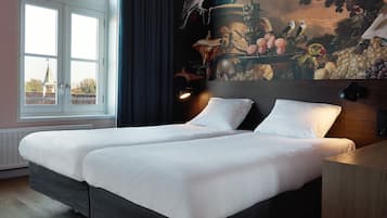 Un lit double avec du linge de lit blanc, une tête de lit sombre et une fresque murale représentant des oiseaux et des fruits.