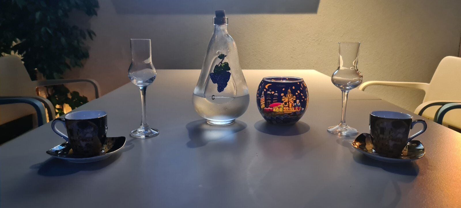 Ein Tisch mit einer Flasche, einer dekorativen Schale und zwei Tassen mit Untertassen.