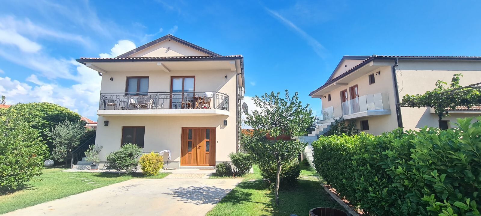 A two-story residential building with a balcony, a front door, and a small garden area.