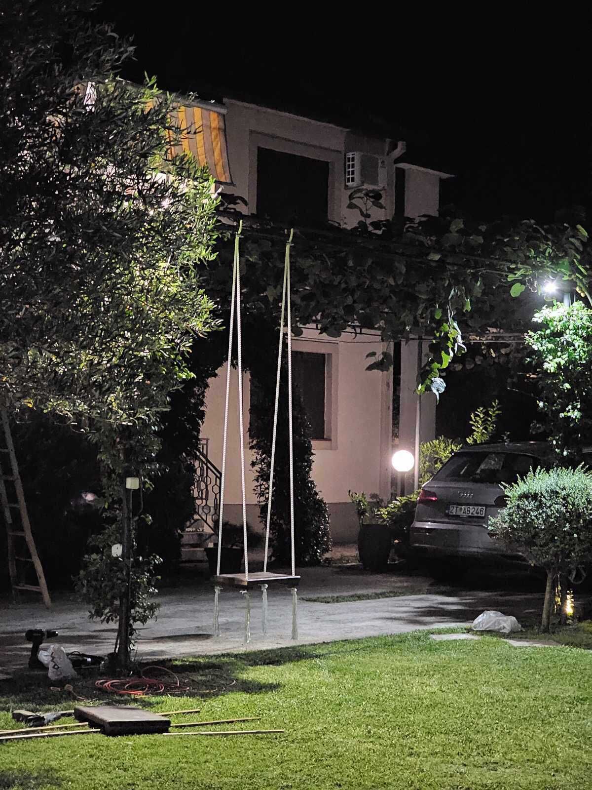 Un barrio residencial de noche con un columpio, un coche aparcado y una casa con una ventana iluminada.