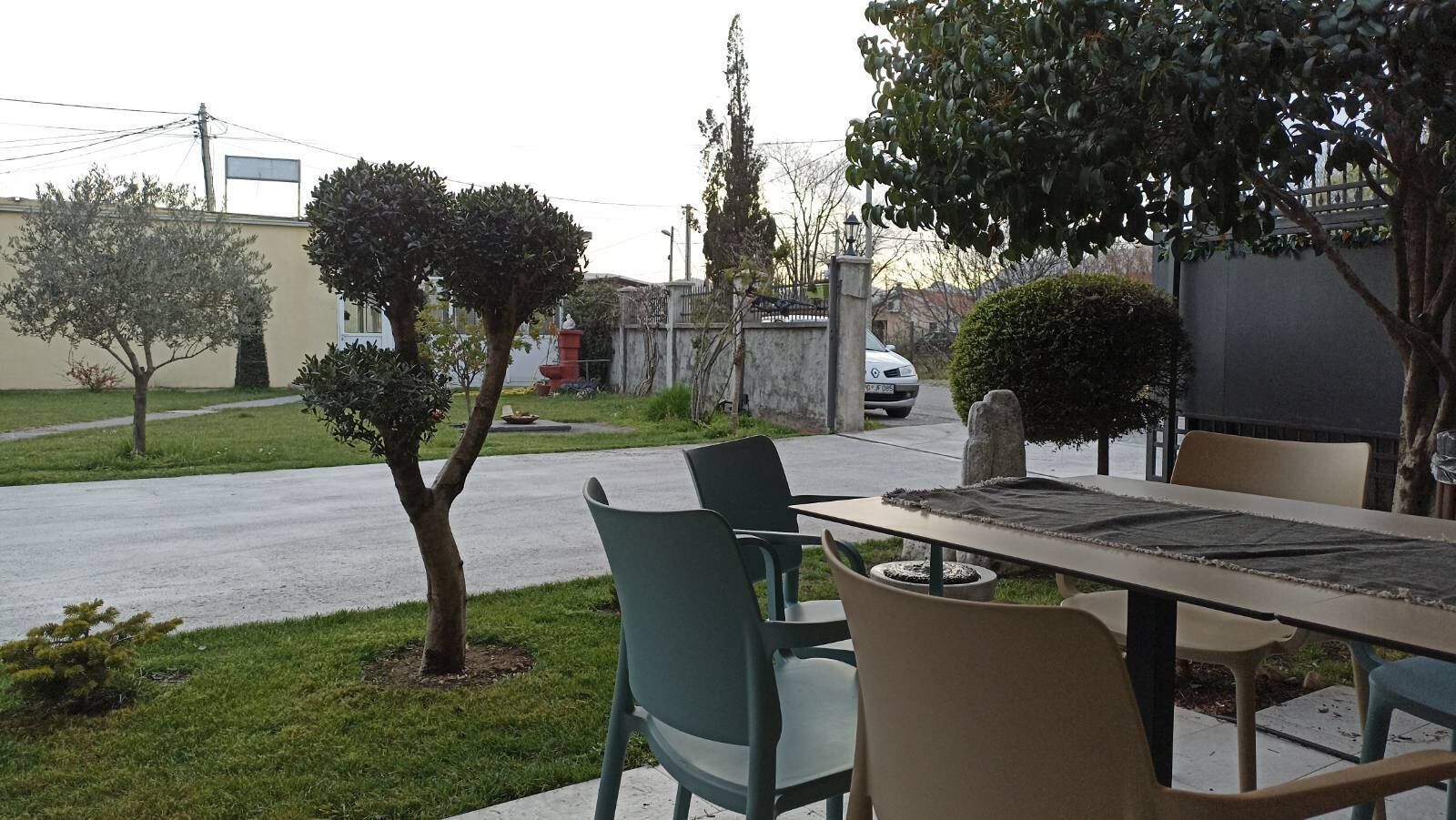 An outdoor seating area with a table and chairs, a small tree, and a parked car in the background.