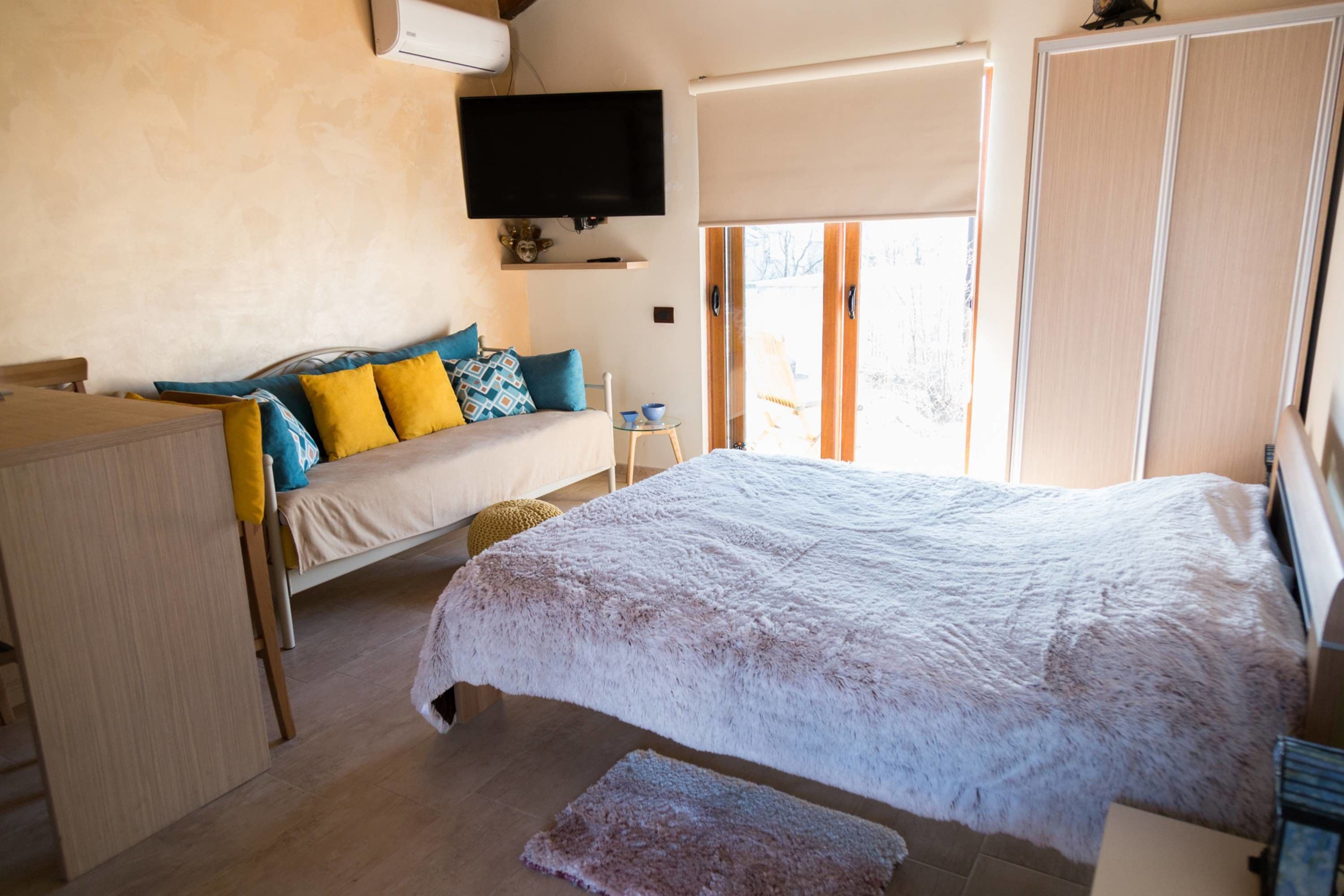 Ein Schlafzimmer mit einem großen Bett, einem an der Wand montierten Fernseher und einer Schiebetür, die auf einen Balkon führt.